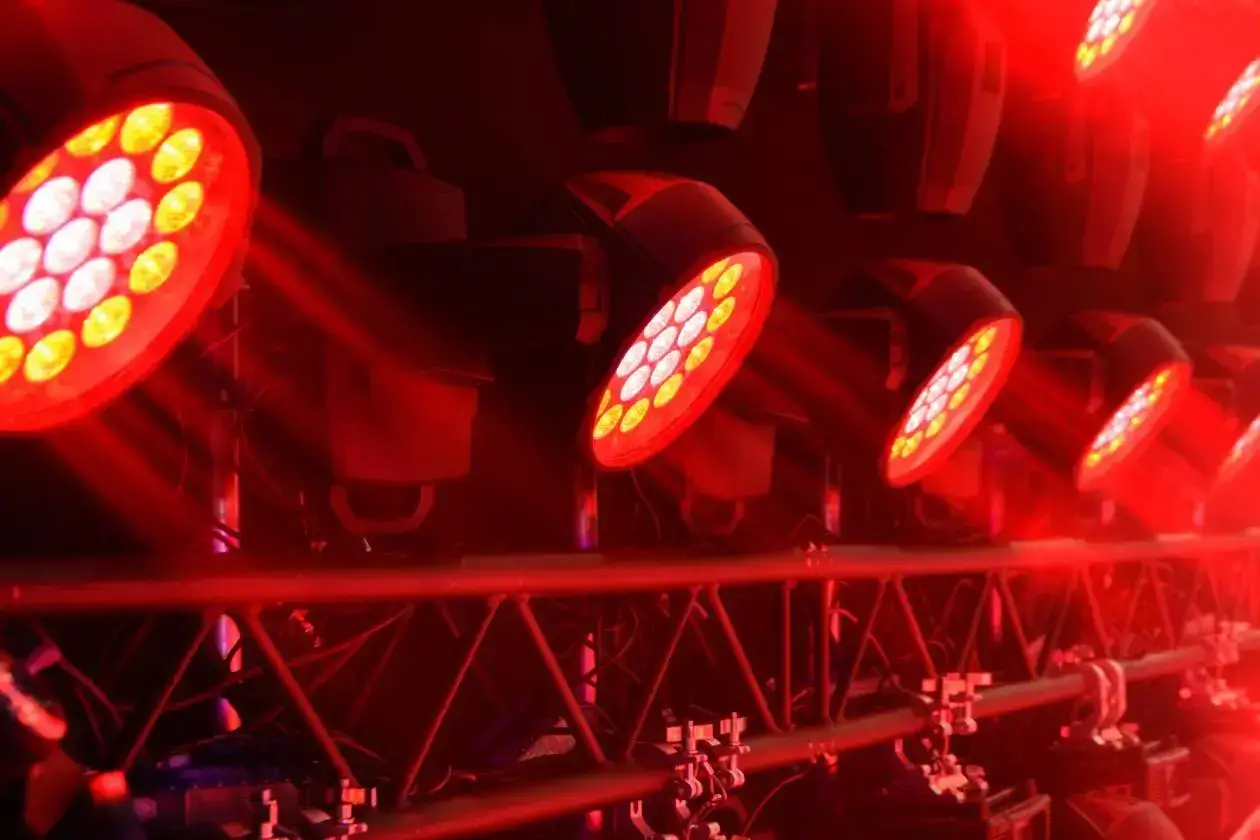 Close-up of stage LED wash lights mounted on a truss, glowing bright red with beams of light shining forward.